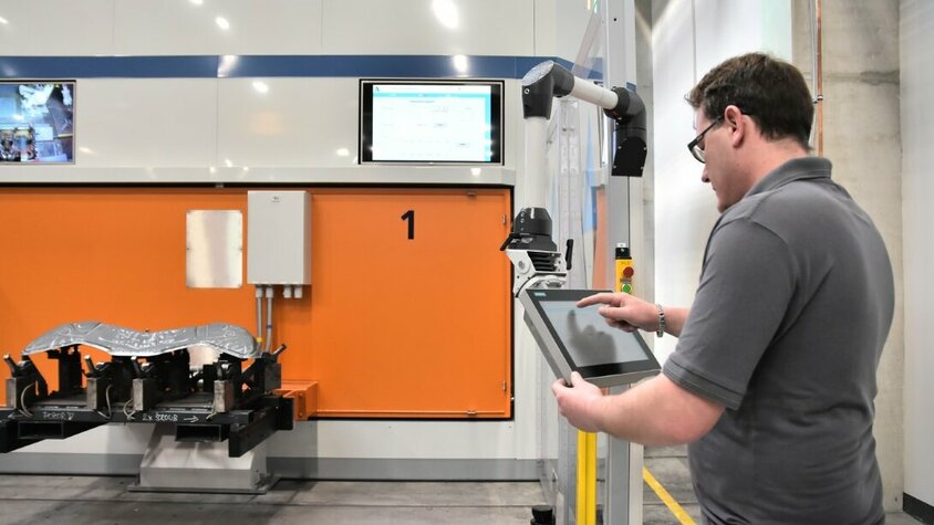 Werkzeugherstellung - Laserprozess bei weba Werkzeugbau Ein Lasertechniker programmiert die im Hintergrund zu sehende Laserschneidanlage auf einem Tablet