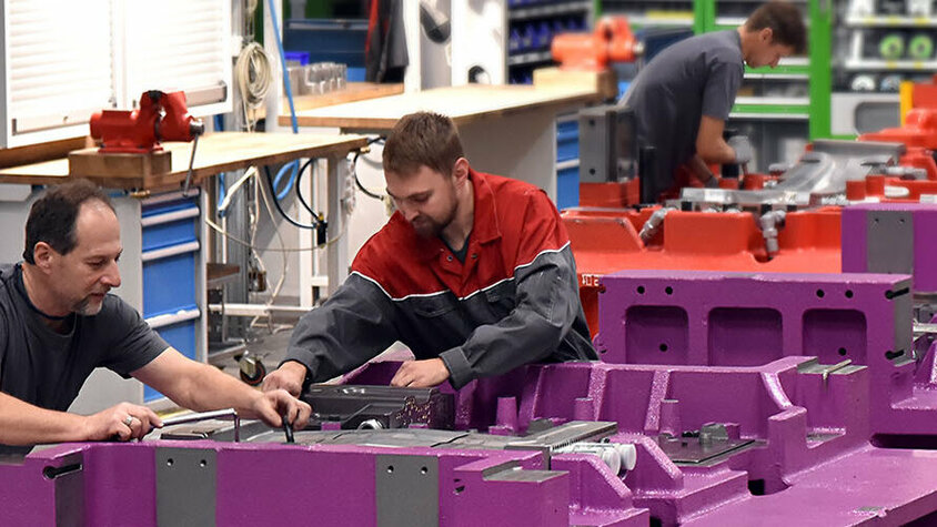 Werkzeugherstellung - High-tech Werkzeugbau Die Aufnahme zeigt Werkzeugbautechniker von weba, die sich konzentriert mit dem Zusammenbau von Warmumformwerkzeugen beschäftigen. Die Techniker arbeiten mit Präzision und Sorgfalt, während sie verschiedene Komponenten der Werkzeuge montieren. Die Szene strahlt Professionalität und Fachkompetenz aus und verdeutlicht die anspruchsvolle Handwerkskunst, die für die Werkzeugherstellung hochwertiger Umformwerkzeuge erforderlich ist.