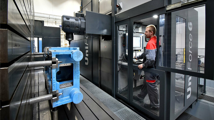 Mechanische Bearbeitung im Presshärten - Höchste Präzision und Expertise bei weba Werkzeugbau in Olomouc Der Maschinenbediener steht konzentriert im Bedienraum des Bearbeitungszentrums und überwacht den Bearbeitungsprozess eines großen Gusses. Sein Blick ist auf das Werkstück gerichtet, während er die Maschine steuert und mögliche Anpassungen vornimmt. Die Szene vermittelt den Eindruck von Fachkompetenz und Präzision in der Fertigungsumgebung.