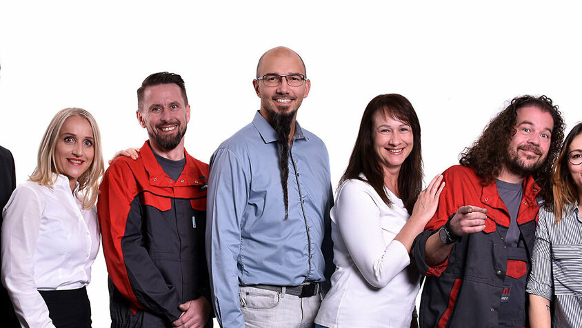 Jobs in Steyr - Arbeitskultur bei weba Werkzeugbau Gruppe von sieben weba Werkzeugbau Mitarbeitenden aus verschiedenen Abteilungen, posierend für ein gemeinsames Foto. Zwei tragen typische Arbeitskleidung, symbolisch für die Fertigungsbereiche. Zwei weitere sind in formeller Business-Kleidung, repräsentativ für Management- oder Bürofunktionen. Die restlichen drei Mitarbeiterinnen und Mitarbeiter präsentieren sich in legerem Casual-Look, was auf kreative oder weniger formelle Rollen im Unternehmen hindeutet. Die Vielfalt an Kleidungsstilen spiegelt die Bandbreite der Berufsrollen und die inklusive Arbeitskultur bei weba wider. Das Bild präsentiert Arbeitskultur und Jobs in Steyr bei weba Werkzeugbau.