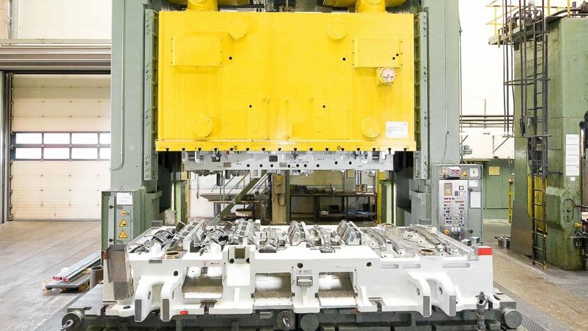 weba Werkzeugbau - Effizienzsteigerung durch Exzenterpresse Exzenter- bzw. Vierpunkt-Kurbelpresse mit ausgefahrenem Pressentisch, auf dem ein großes weißes Linienwerkzeug eingespannt ist.