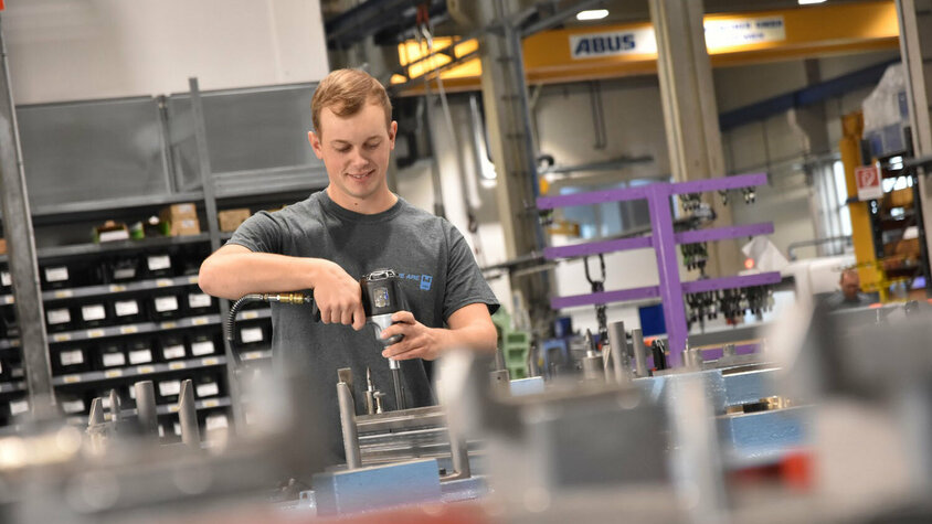 Praktikum Jobs in Steyr - Technische Erfahrung in der Metalltechnik Junger lächelnder Werkzeugmacher in einer Produktionsumgebung beim Montieren eines Umformwerkzeugs in seinem Praktikum Job in Steyr bei weba.