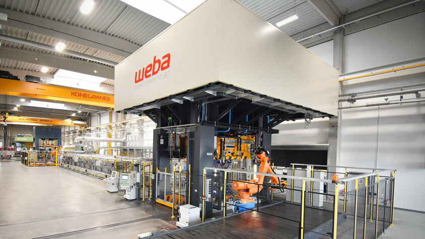 weba Werkzeugbau - Serienfertigung in der Warmumformung Umformpresse und Auslaufband einer Warmumformlinie. Die industrielle Umgebung zeigt moderne Maschinen und präzise Technik, die in der Warmumformung zum Einsatz kommen.