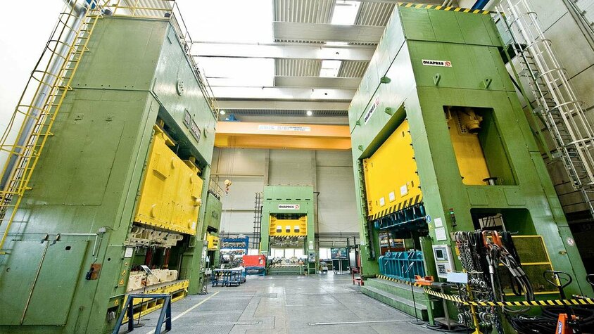 Stanz- und Umformwerkzeuge - Hydraulische und Mechanische Pressen für optimales Werkzeug-Tryout Das Bild zeigt das Pressenhaus von weba Werkzeugbau in Dietach. Im Vordergrund befinden sich eine Exzenter- und eine hydraulische Presse, während in der Mitte eine weitere hydraulische Umformpresse positioniert ist. Die Pressen sind bereit für die Umformung von Metallteilen und vermitteln den Eindruck von Kraft und Präzision in der Produktion. Die Szene strahlt eine industrielle Atmosphäre aus und zeigt die fortgeschrittene Technologie und Ausrüstung des Unternehmens in der Herstellung von Stanz- und Umformwerkzeugen..