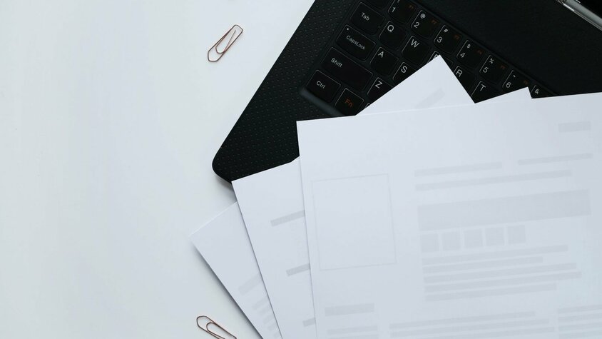 Karriere-Ratgeber der weba Werkzeugbau - Tipps für das Schreiben eines Lebenslaufs Lose Blätter eines Lebenslaufes liegen auf einer schwarzen Tastatur, umgeben von Büroklammern.