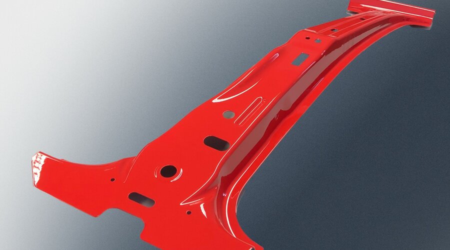 Metal component from the prototype manufacturing process at weba Deutschland, painted red, featuring a complex geometry with multiple cutouts, set against a dark background.