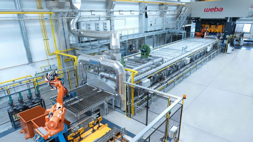 Presshärten - Serienfertigung und Digitale Qualitätskontrolle bei weba Werkzeugbau in Olomouc Das Bild zeigt eine Gesamtaufnahme der Presshärtelinie von weba Olomouc. Alle Prozessschritte im Presshärten sind deutlich zu erkennen: von der Markierstation über den Transfer zum Ofen, den Transfer vom Ofen in die Presse bis hin zur Umformpresse.