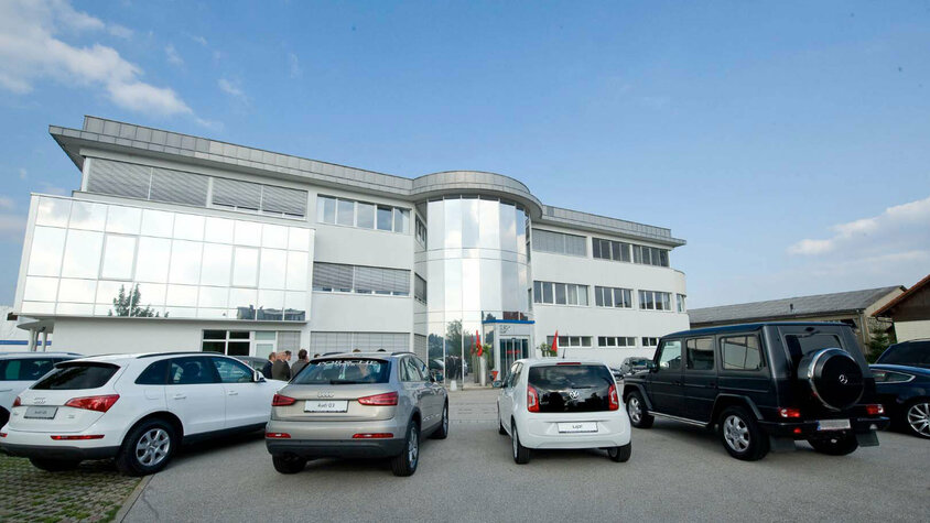 weba Werkzeugbau - Jubiläumsfeier Automeile Außenaufnahme der weba Werkzeugbau mit mehreren namhaften Automarken davor parkiert, moderner Gebäudekomplex unter einem klaren Himmel.