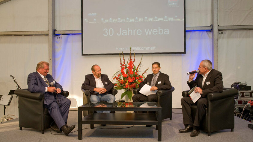 weba Werkzeugbau - Jubiläumsfeier und Interview der Unternehmensgründer Unternehmensgründer Danzinger Herbert und Wolfgang Haidenthaler sowie Geschäftsführer Hannes Feuerhuber gemeinsam mit dem Event-Moderator auf der Bühne bei der 30-Jährigen Jubiläumsfeier, vor feierlichem Hintergrund.