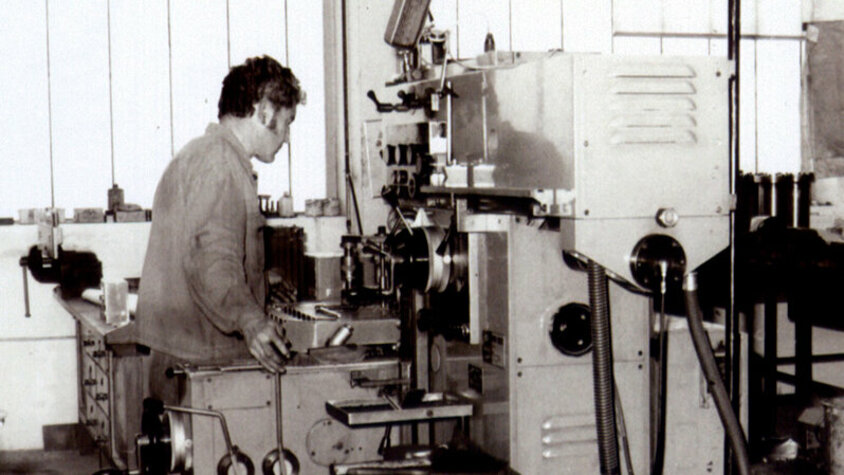 weba Werkzeugbau - Anfangsjahre als kleiner Formen- und Werkzeugbau Ein Schwarz-Weiß-Bild aus den 80er Jahren zeigt einen Zerspanungstechniker, der ein konventionelles Bohrwerk bedient.