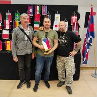 František Krumpolec stands with two fellow model builders in front of an exhibition display with international flags.
