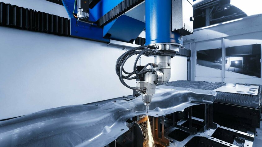 Hochpräzises Laserschneiden in der Fertigung von Automobilteilen Präzise Laserschneidmaschine bei der Bearbeitung eines Bauteils. Die Maschine schneidet mit hoher Genauigkeit durch ein komplex geformtes Metallteil und erzeugt dabei Funken. Moderne Laserschneidtechnologie für die Fertigung von Automobilkomponenten.