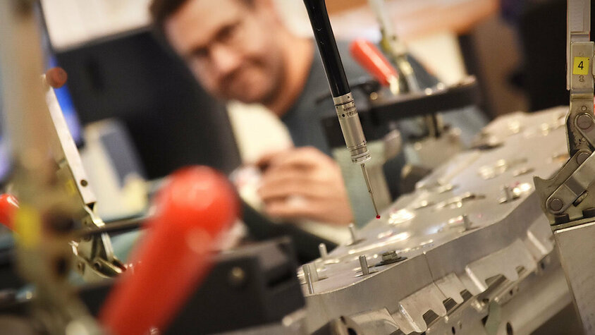 Messtechnik - 3D-Koordinantenmessung und taktile Messsysteme Nahaufnahme einer Koordinatenmessmaschine mit Fokus auf den Messtaster. Im Hintergrund ist der Messtechniker unscharf und verschwommen zu sehen.