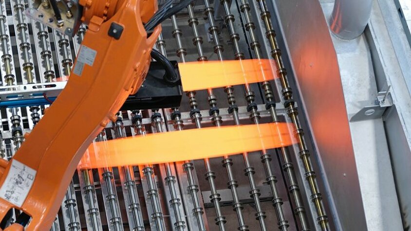 Prozesstechnik für das Presshärten bei weba Werkzeugbau Industrieller Roboterarm in der Prozesstechnik für das Presshärten positioniert glühend heiße Metallbleche auf einer Produktionsanlage. Der Einsatz modernster Technologie optimiert den Presshärteprozess und gewährleistet eine präzise Steuerung der Umformprozesse bei weba Werkzeugbau.