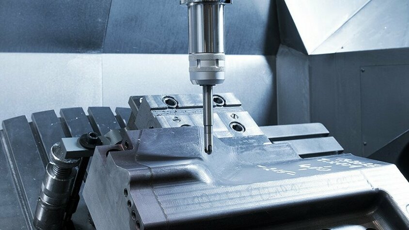 CNC-Fräsen eines Stahleinsatzes in der Lohnfertigung Innenaufnahme eines CNC-Bearbeitungszentrums bei der Lohnfertigung, während es einen Stahleinsatz fräst.