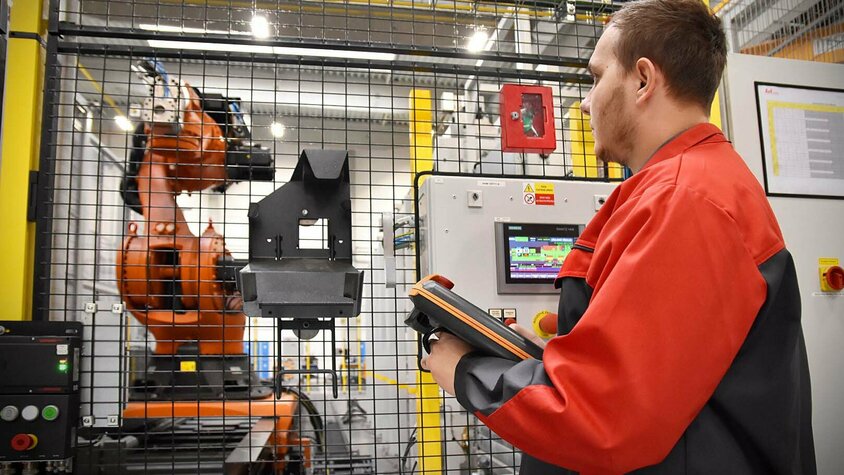 Presshärten - Flexible Fertigung durch Automatisierung bei weba Werkzeugbau in Olomouc Ein Zerspanungstechniker programmiert die automatisierte Zerspanungslinie von weba Olomouc. Konzentriert betrachtet er den Transfergreifer, während er ein Bedientablet in den Händen hält.