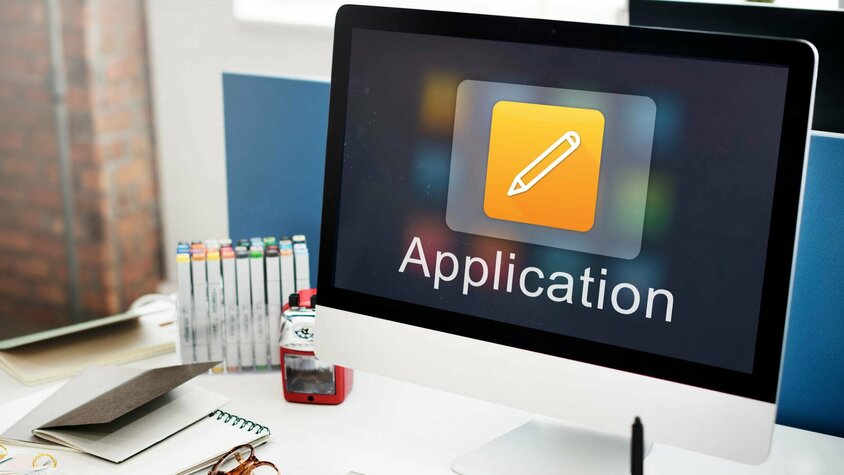 Stellenangebote in Steyr - Initiativbewerbung bei weba Werkzeugbau Schreibtisch mit Apple Bildschirm, Tastatur und Büromaterialien. Auf dem Bildschirm ist das Wort "Application" zu sehen, dass Symbolisch für Stellenangebote in Steyr bei weba Werkzeugbau steht.